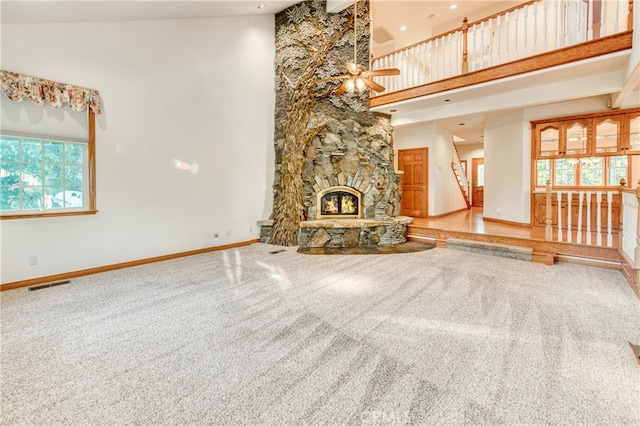 unfurnished living room with ceiling fan, a wealth of natural light, a fireplace, and a high ceiling