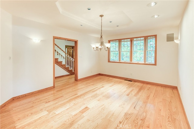 empty room with an inviting chandelier, light hardwood / wood-style flooring, and a tray ceiling