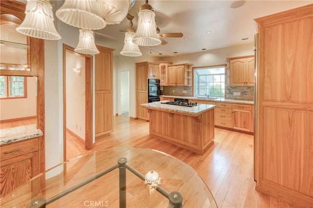 kitchen with a kitchen island, light hardwood / wood-style floors, ceiling fan, backsplash, and light stone counters