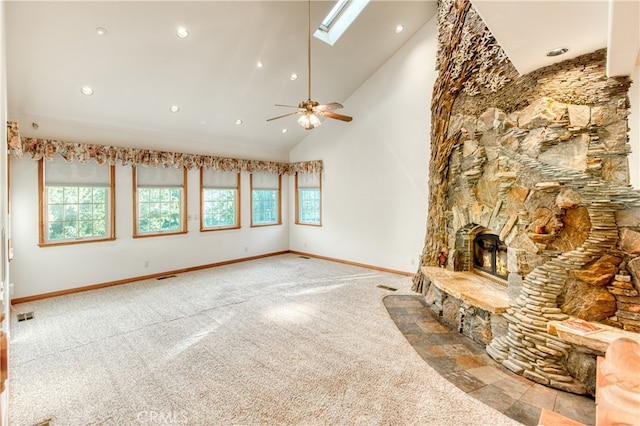 unfurnished living room featuring ceiling fan, a healthy amount of sunlight, a skylight, and a fireplace