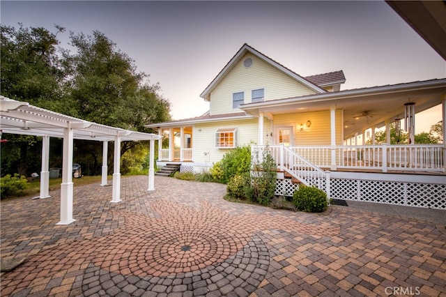 back house at dusk with a patio area, a porch, and a pergola