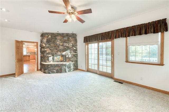 unfurnished living room featuring ceiling fan, carpet floors, and a stone fireplace