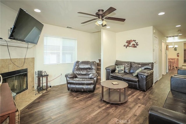 living room with a tile fireplace, dark wood-type flooring, and ceiling fan with notable chandelier