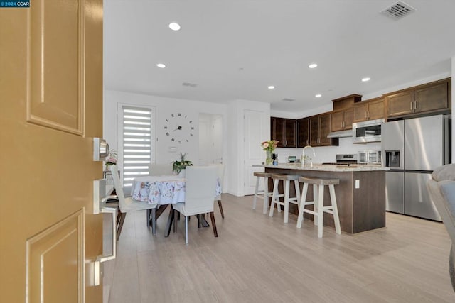 kitchen with light hardwood / wood-style floors, a kitchen island with sink, a kitchen bar, appliances with stainless steel finishes, and sink