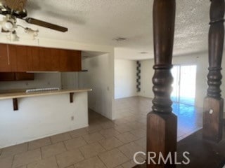 kitchen featuring a kitchen bar, tile patterned floors, a textured ceiling, kitchen peninsula, and ceiling fan