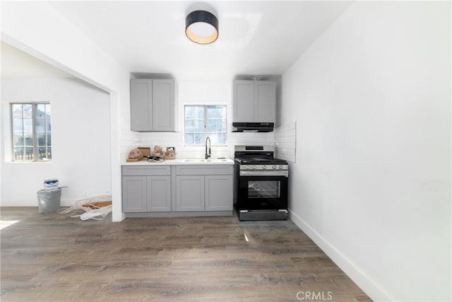 kitchen with stainless steel gas range, sink, gray cabinetry, dark hardwood / wood-style floors, and backsplash