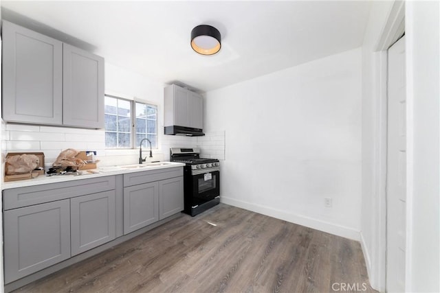 kitchen with gray cabinets, stainless steel range with gas cooktop, sink, backsplash, and hardwood / wood-style flooring