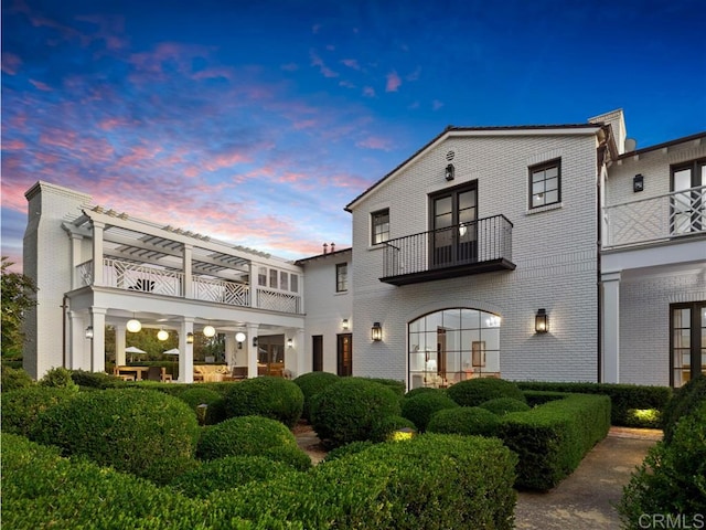 back of house at dusk featuring brick siding and a balcony