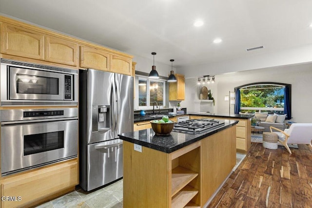 kitchen with sink, stainless steel appliances, a kitchen island, decorative light fixtures, and dark stone counters