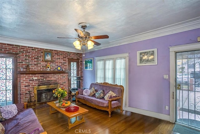 living room featuring ceiling fan, wood-type flooring, a brick fireplace, and crown molding