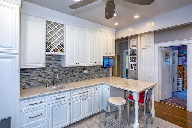 kitchen featuring ceiling fan, a kitchen bar, sink, light stone countertops, and white cabinets