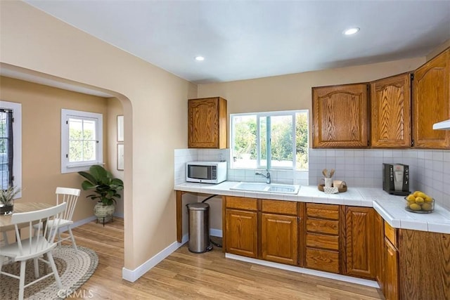 kitchen with light wood-type flooring, decorative backsplash, sink, and tile countertops