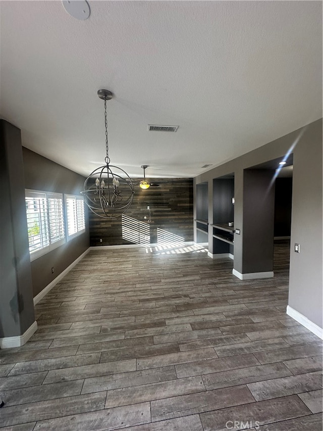 unfurnished living room featuring a textured ceiling, an inviting chandelier, and dark hardwood / wood-style floors