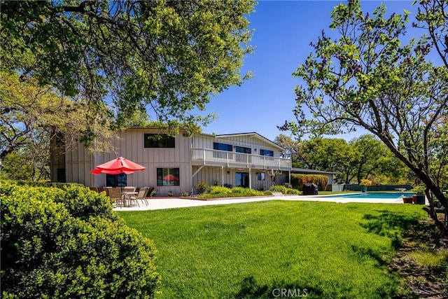 rear view of property featuring a lawn, a balcony, and a patio