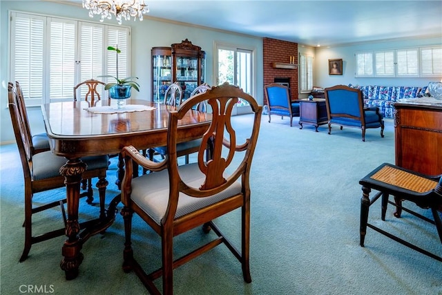 dining space featuring ornamental molding, a fireplace, light carpet, and an inviting chandelier