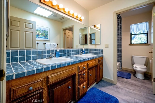 full bathroom with a skylight, wood-type flooring, toilet, decorative backsplash, and vanity