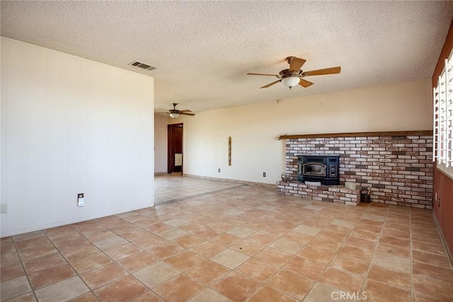 unfurnished living room featuring a wood stove, ceiling fan, light tile patterned flooring, and a textured ceiling