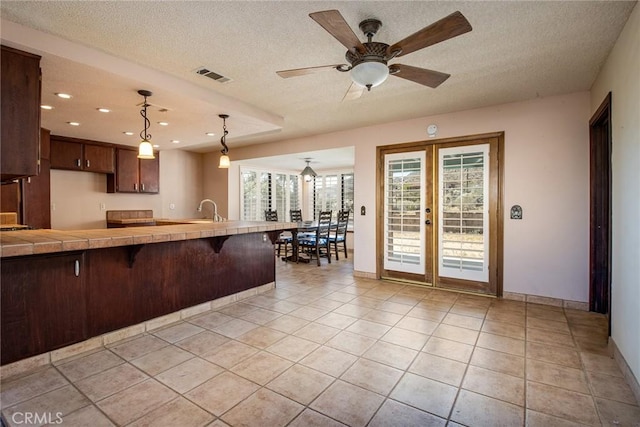 kitchen with a breakfast bar, a textured ceiling, ceiling fan, light tile patterned floors, and hanging light fixtures