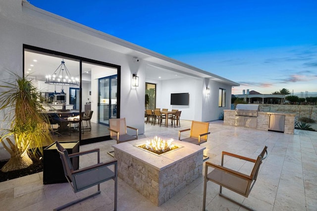 patio terrace at dusk featuring a fire pit and area for grilling