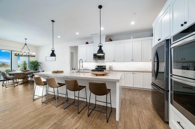 kitchen with light hardwood / wood-style floors, stainless steel appliances, backsplash, white cabinets, and pendant lighting