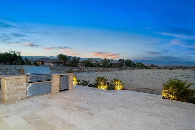 patio terrace at dusk with exterior kitchen and area for grilling