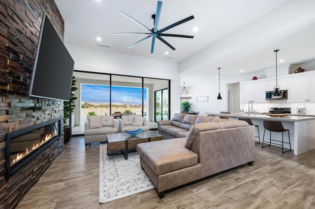 living room with a stone fireplace, ceiling fan, light wood-type flooring, and sink