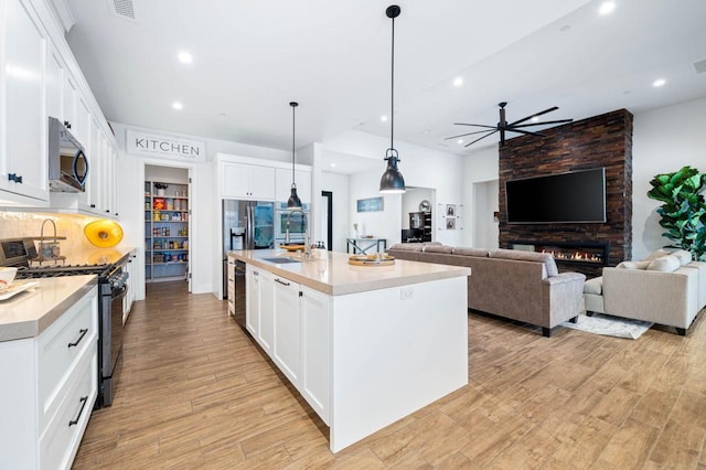 kitchen featuring a large fireplace, ceiling fan, white cabinetry, gas stove, and light wood-type flooring