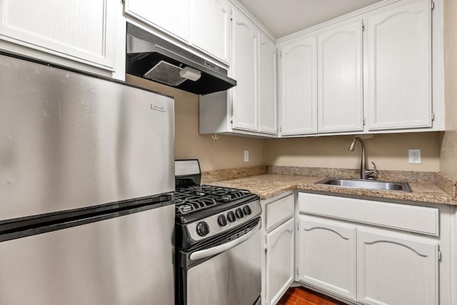 kitchen with gas range, white cabinetry, sink, light stone counters, and stainless steel fridge