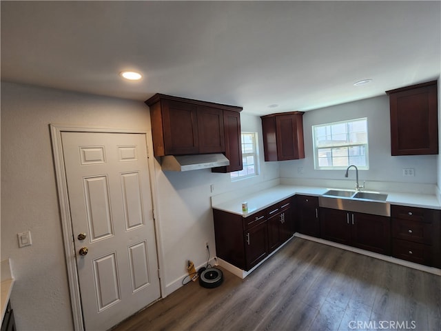 kitchen featuring wall chimney range hood, sink, dark brown cabinets, and dark hardwood / wood-style flooring