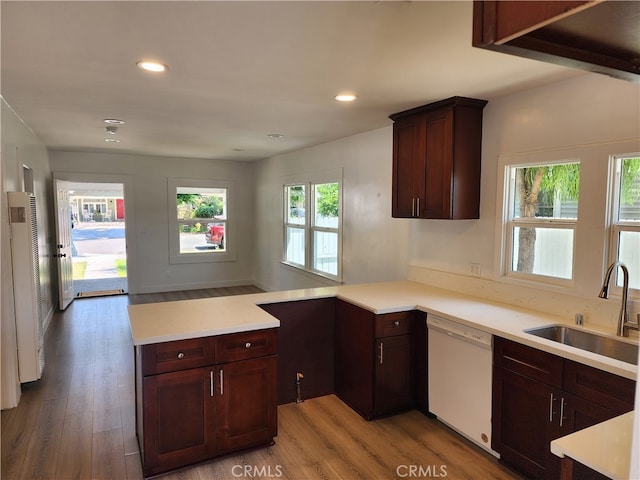 kitchen with kitchen peninsula, hardwood / wood-style flooring, dark brown cabinets, white dishwasher, and sink