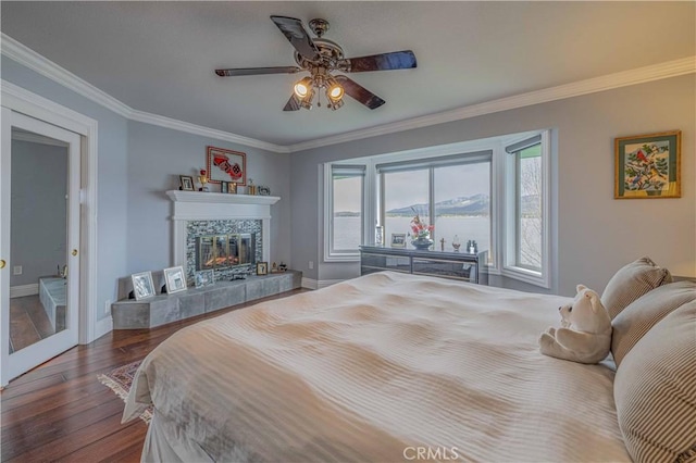 bedroom with a tiled fireplace, ceiling fan, ornamental molding, and hardwood / wood-style floors