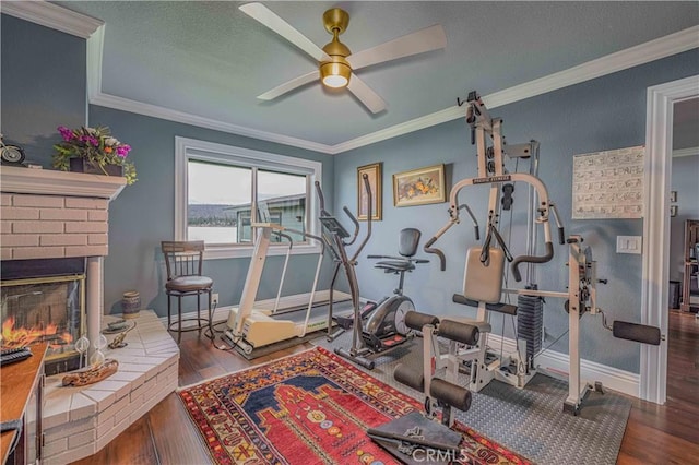 exercise room with ceiling fan, dark hardwood / wood-style floors, crown molding, and a fireplace