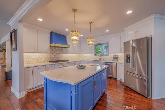 kitchen with pendant lighting, white cabinets, wall chimney exhaust hood, stainless steel appliances, and blue cabinetry