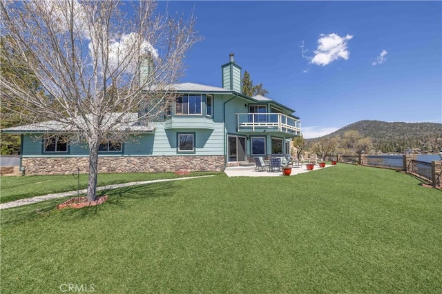 back of property with a yard, a patio area, a mountain view, and a balcony