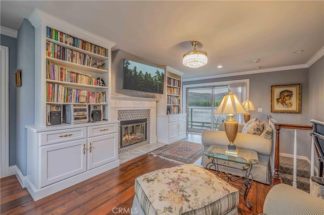 living area with built in shelves, dark hardwood / wood-style floors, crown molding, and a fireplace