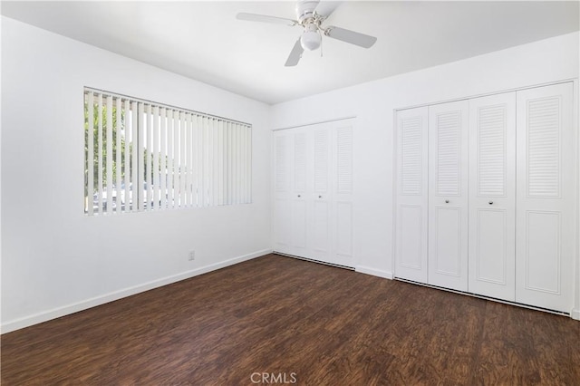 unfurnished bedroom featuring ceiling fan, two closets, and dark hardwood / wood-style floors