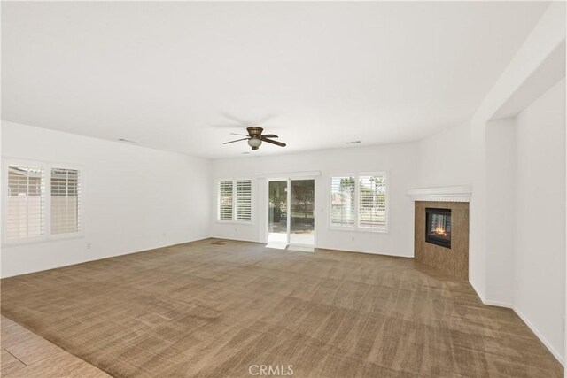 unfurnished living room featuring light colored carpet, ceiling fan, a healthy amount of sunlight, and a tiled fireplace