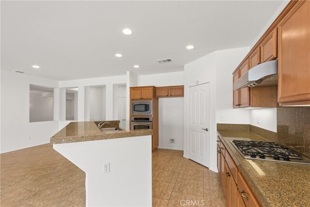 kitchen featuring sink, backsplash, an island with sink, light tile patterned floors, and appliances with stainless steel finishes