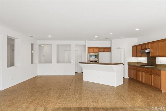 kitchen featuring decorative backsplash, a kitchen island with sink, light tile patterned floors, and stainless steel appliances