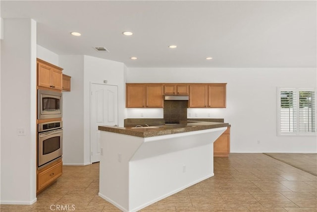 kitchen with stainless steel appliances, an island with sink, and dark stone counters