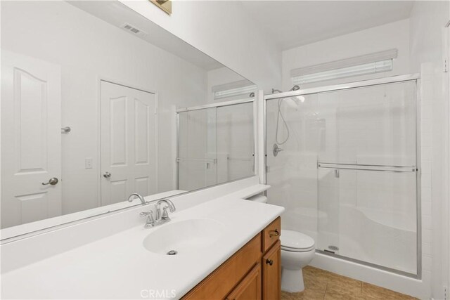 bathroom with tile patterned floors, a shower with door, vanity, and toilet