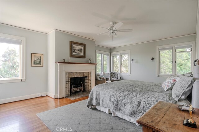 bedroom featuring a brick fireplace, light hardwood / wood-style flooring, multiple windows, and ceiling fan