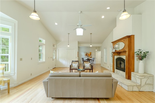 living room with high vaulted ceiling, a fireplace, ceiling fan, and light hardwood / wood-style flooring