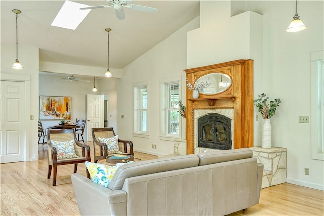 living room with a premium fireplace, baseboards, light wood-type flooring, a ceiling fan, and high vaulted ceiling