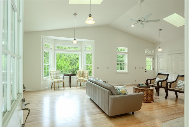 living room featuring high vaulted ceiling, ceiling fan, a skylight, and light hardwood / wood-style flooring