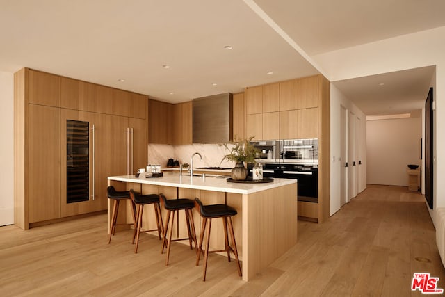 kitchen with light hardwood / wood-style floors, a center island with sink, backsplash, black oven, and a breakfast bar