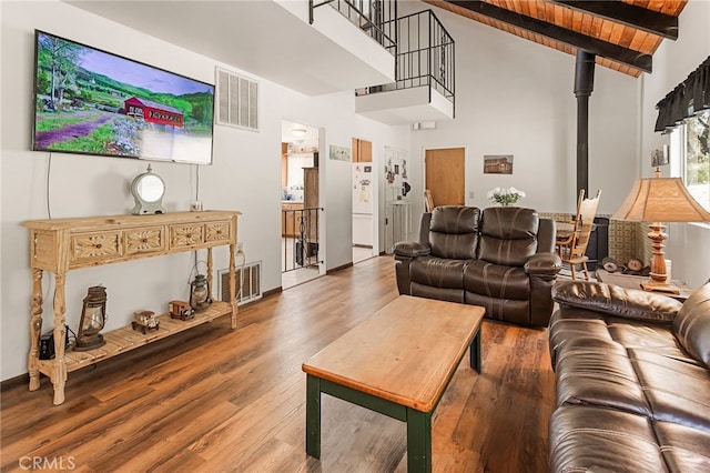 living room featuring high vaulted ceiling, beamed ceiling, wood-type flooring, a wood stove, and wooden ceiling