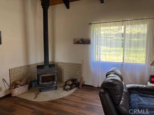 living room featuring dark wood-type flooring, beamed ceiling, and a wood stove