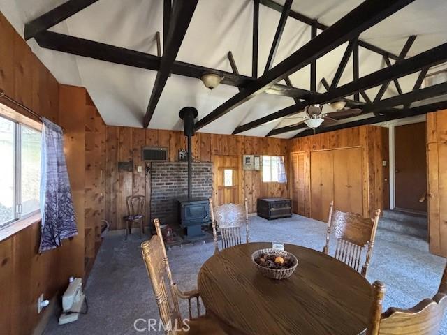 unfurnished dining area featuring lofted ceiling with beams, carpet floors, a wood stove, and wooden walls