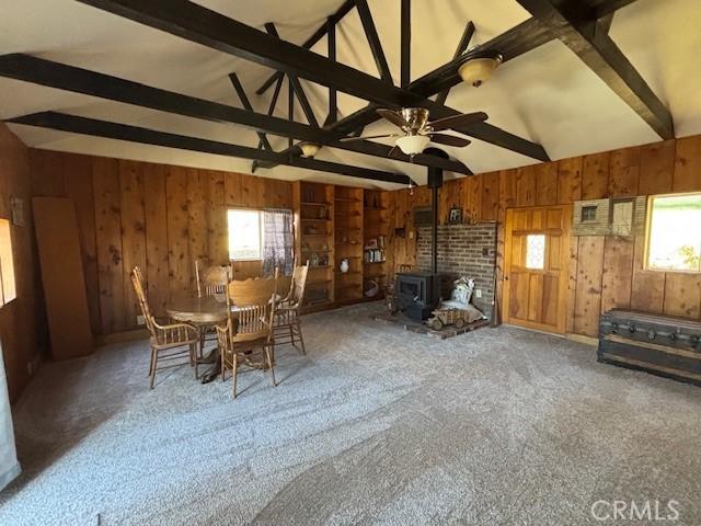 unfurnished dining area featuring carpet floors, a wealth of natural light, beamed ceiling, and a wood stove